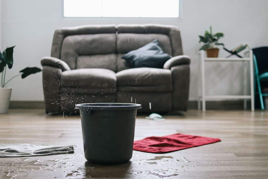 Living room with a bucket catching water from a leaking roof