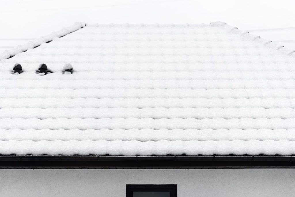 Roof covered with snow against a cloudy sky visible ceramic ventilation fireplace on the roof and falling snow