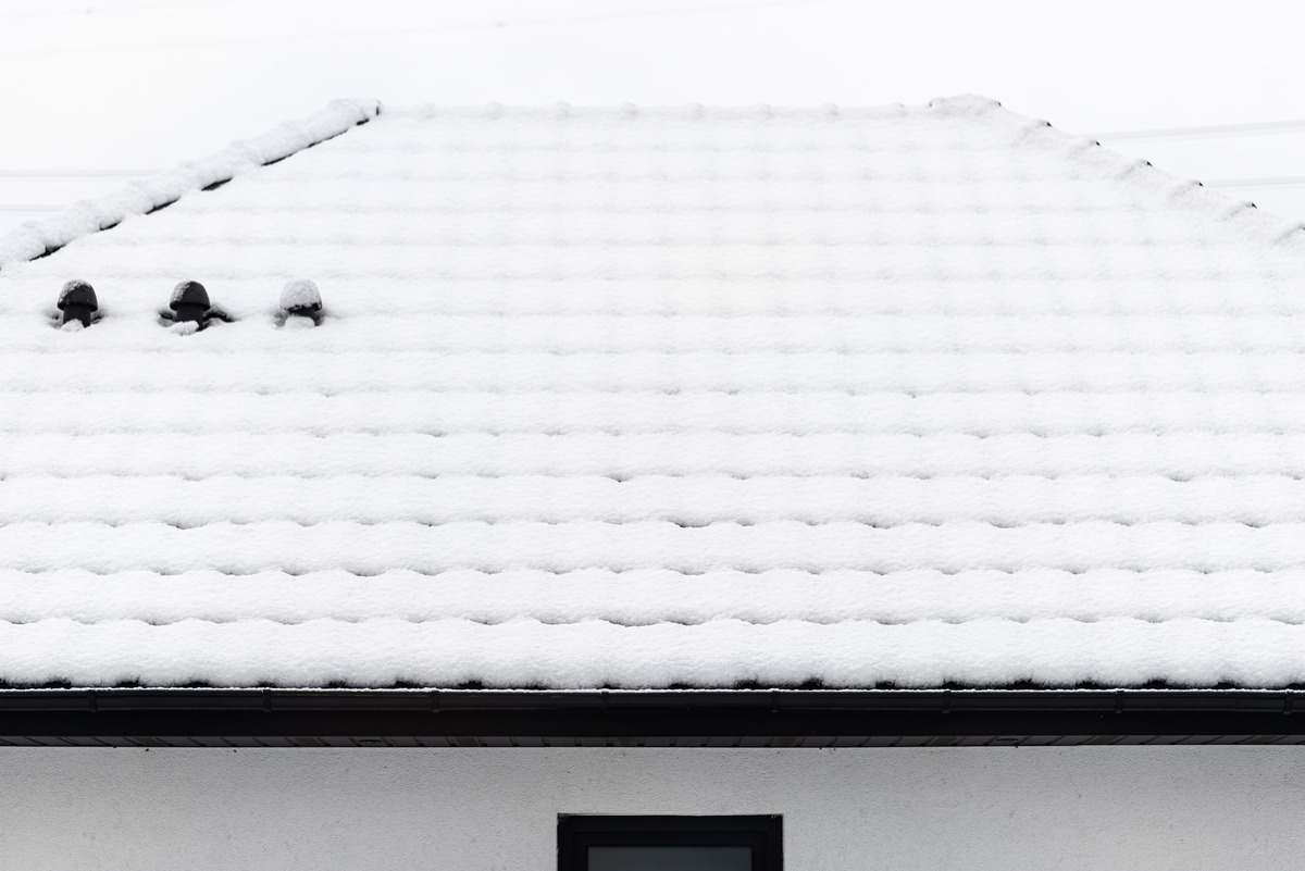 Roof covered with snow against a cloudy sky visible ceramic ventilation fireplace on the roof and falling snow